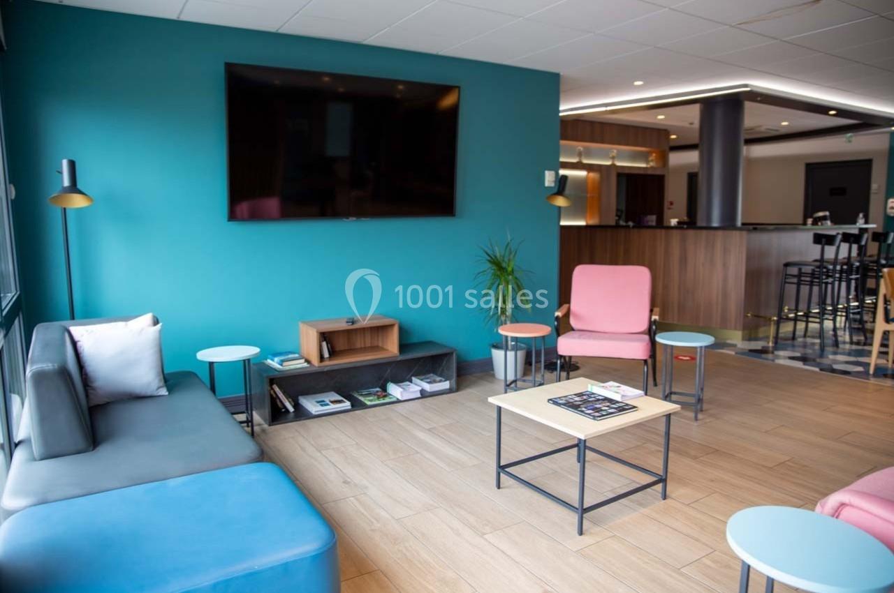 Salon moderne avec canapé, fauteuils colorés, table basse et télévision murale dans un espace lumineux.