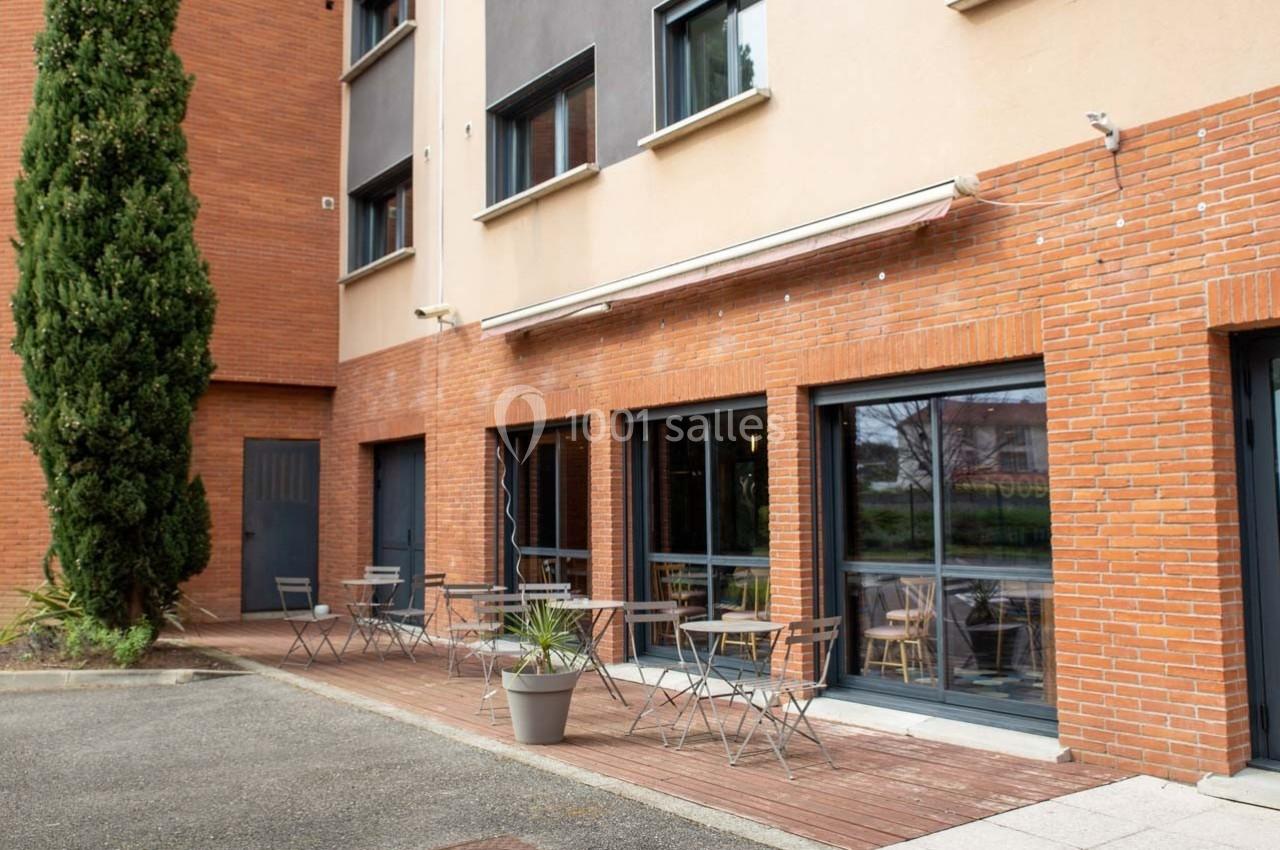 Terrasse extérieure avec tables et chaises en métal devant un bâtiment en briques rouges et beige.