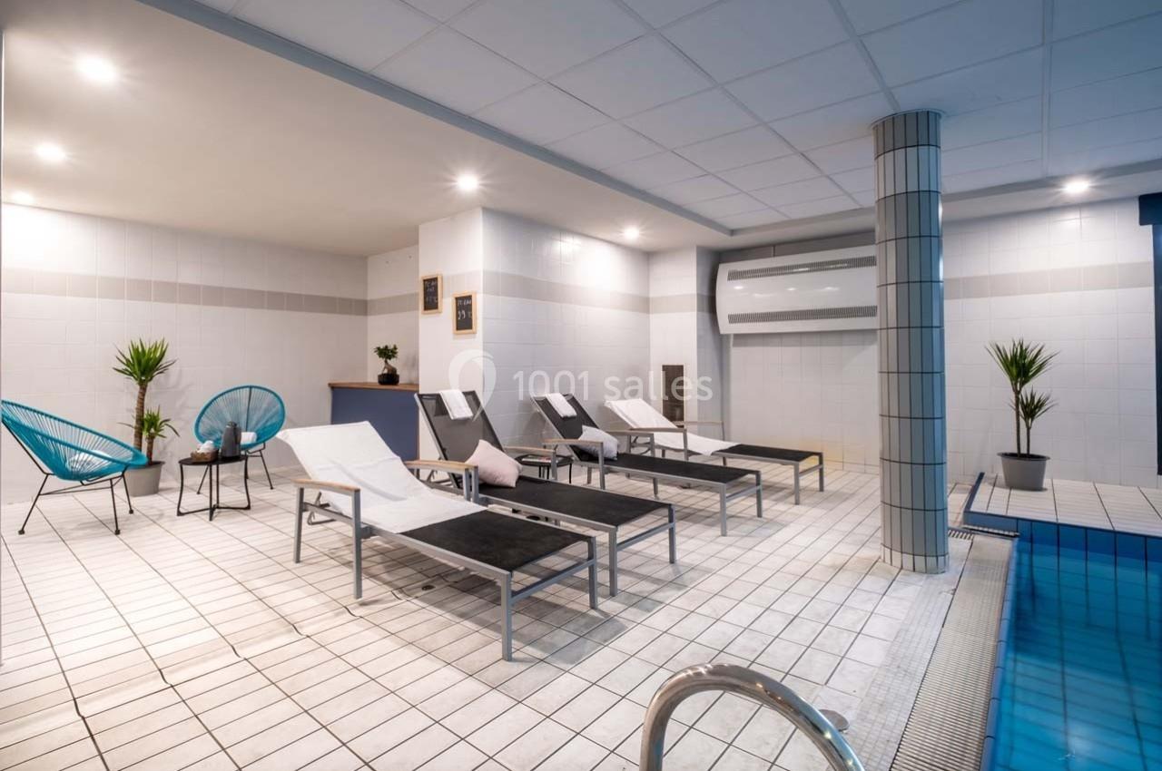 Espace intérieur avec transats alignés près d'une piscine, décoré de plantes et éclairé par des lumières au plafond.