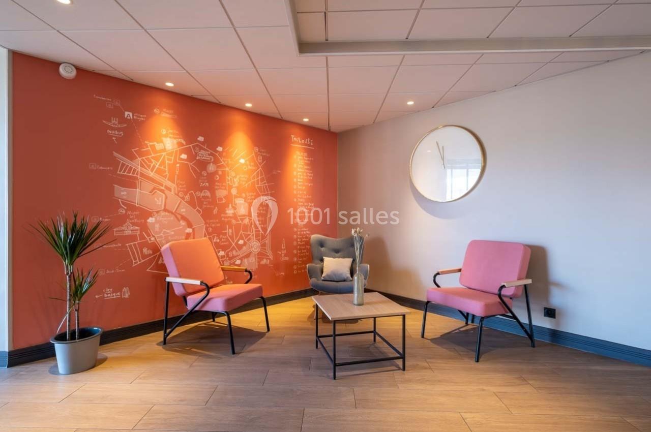 Espace d'attente avec deux fauteuils roses, une table basse, un fauteuil gris et un mur décoré d'une carte illustrée.