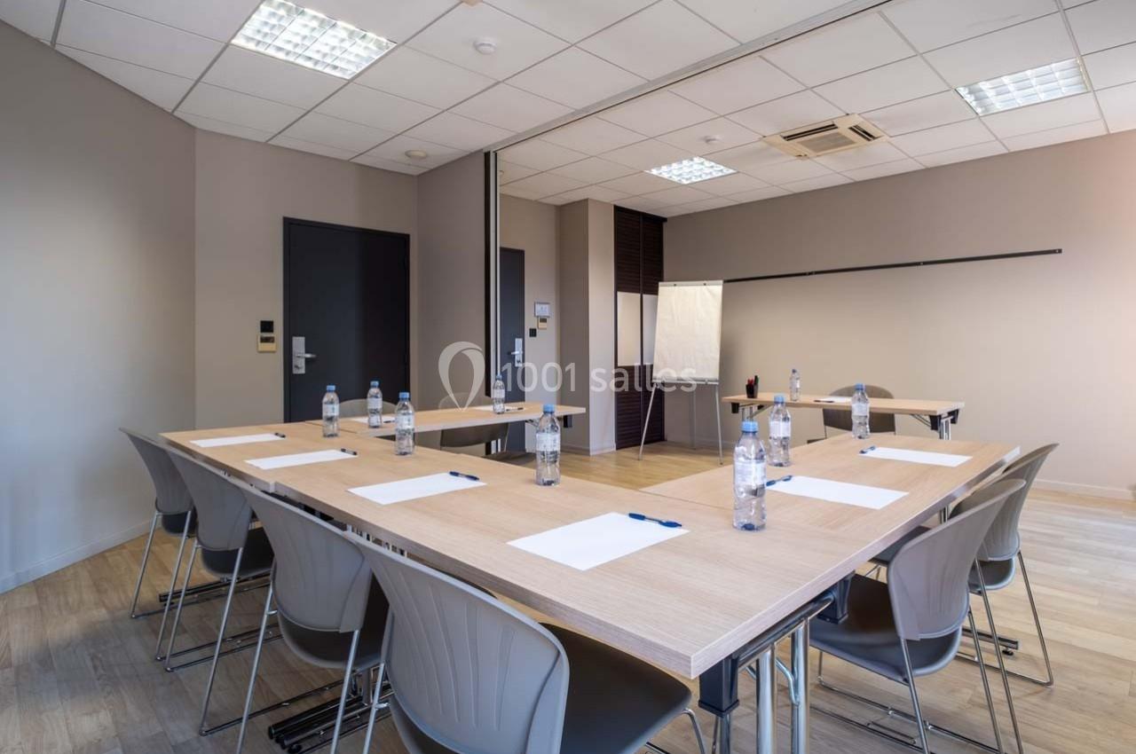 Salle de réunion lumineuse avec tables en U, chaises, bouteilles d'eau, blocs-notes et tableau blanc.