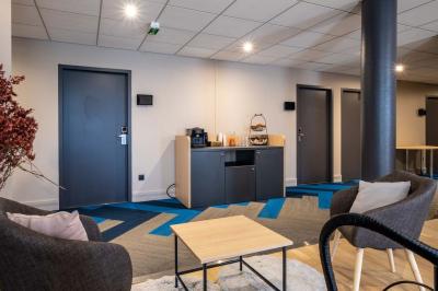 Chambre lumineuse avec lit double, bureau, télévision, machine à café et grande fenêtre offrant une vue extérieure.