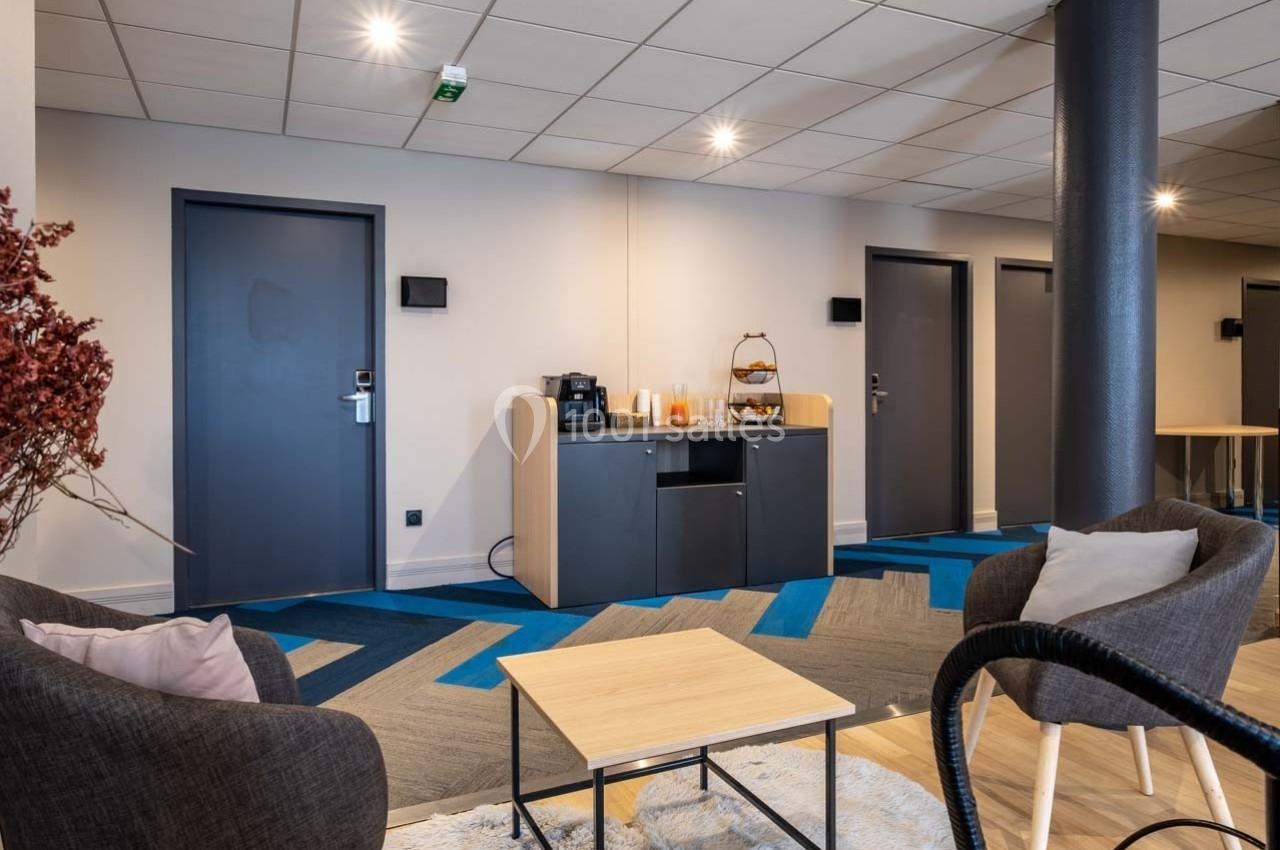 Coin détente avec fauteuils, table basse, et un meuble équipé d'une machine à café et d'un distributeur de boissons.