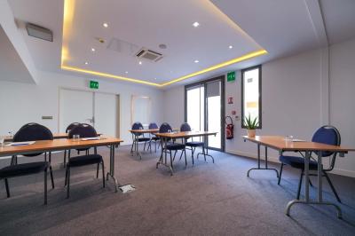 Chambre d'hôtel lumineuse avec un grand lit, des lampes de chevet, un bureau, une télévision et une fenêtre avec rideaux.