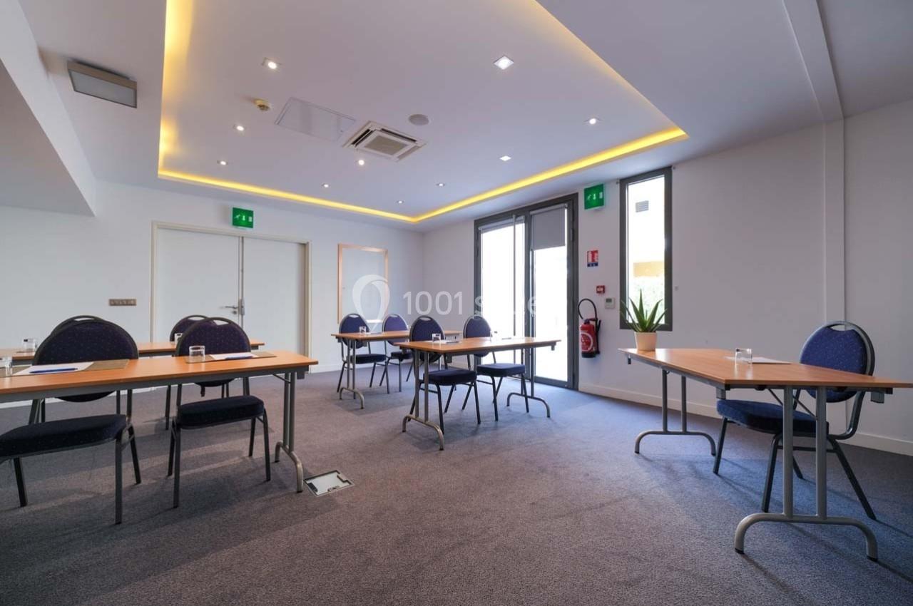 Salle de réunion lumineuse avec des tables espacées, des chaises, des verres et des documents, éclairage moderne au plafond.