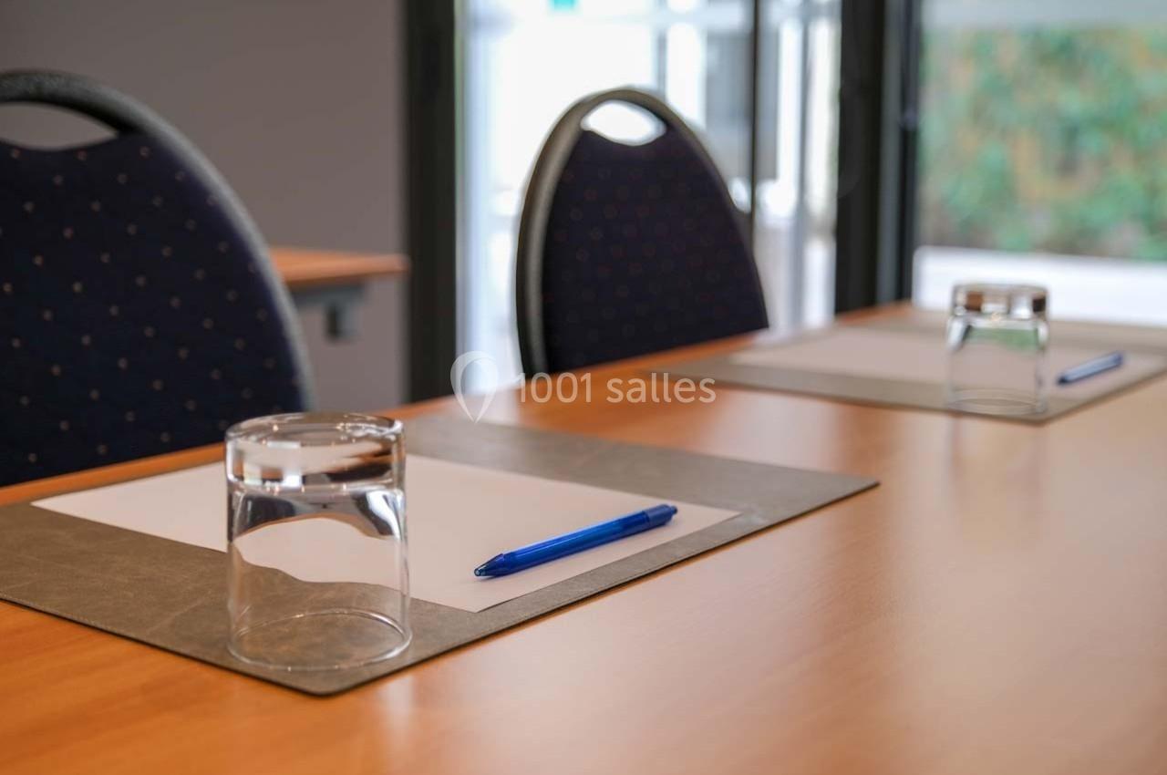Deux verres, des stylos et des blocs-notes disposés sur une table en bois dans une salle de réunion lumineuse.