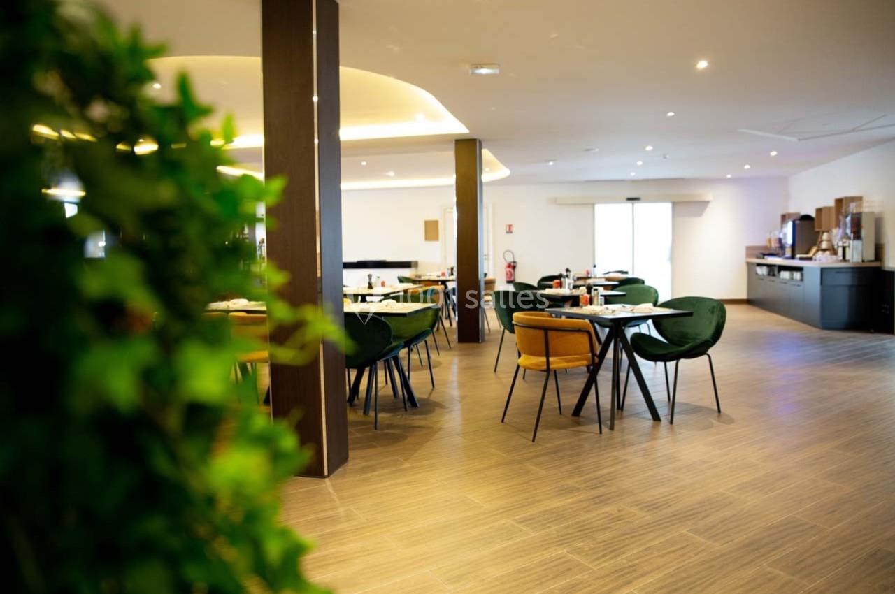 Salle de restaurant lumineuse avec tables dressées, chaises colorées et un coin buffet en arrière-plan.