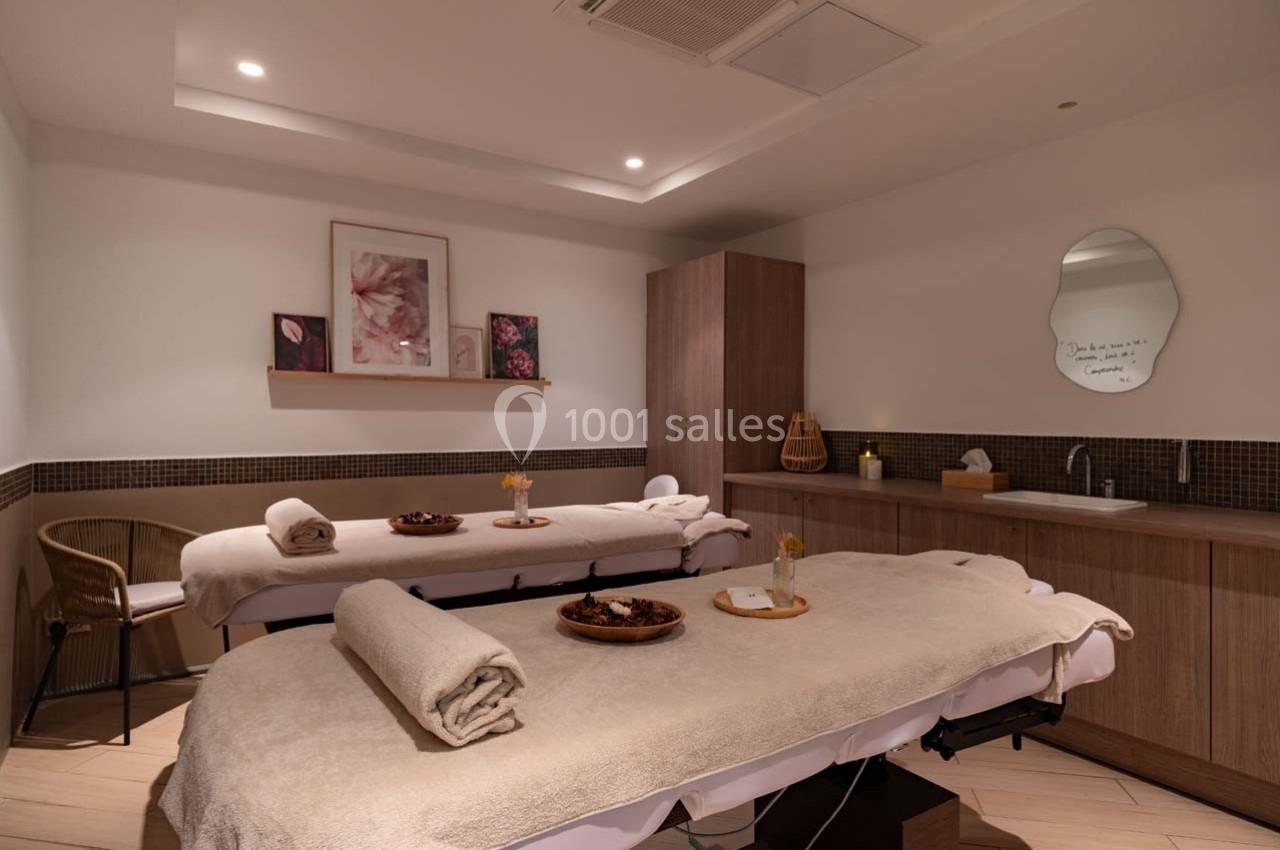 Deux tables de massage avec serviettes et décor apaisant dans une salle lumineuse et aménagée pour des soins.