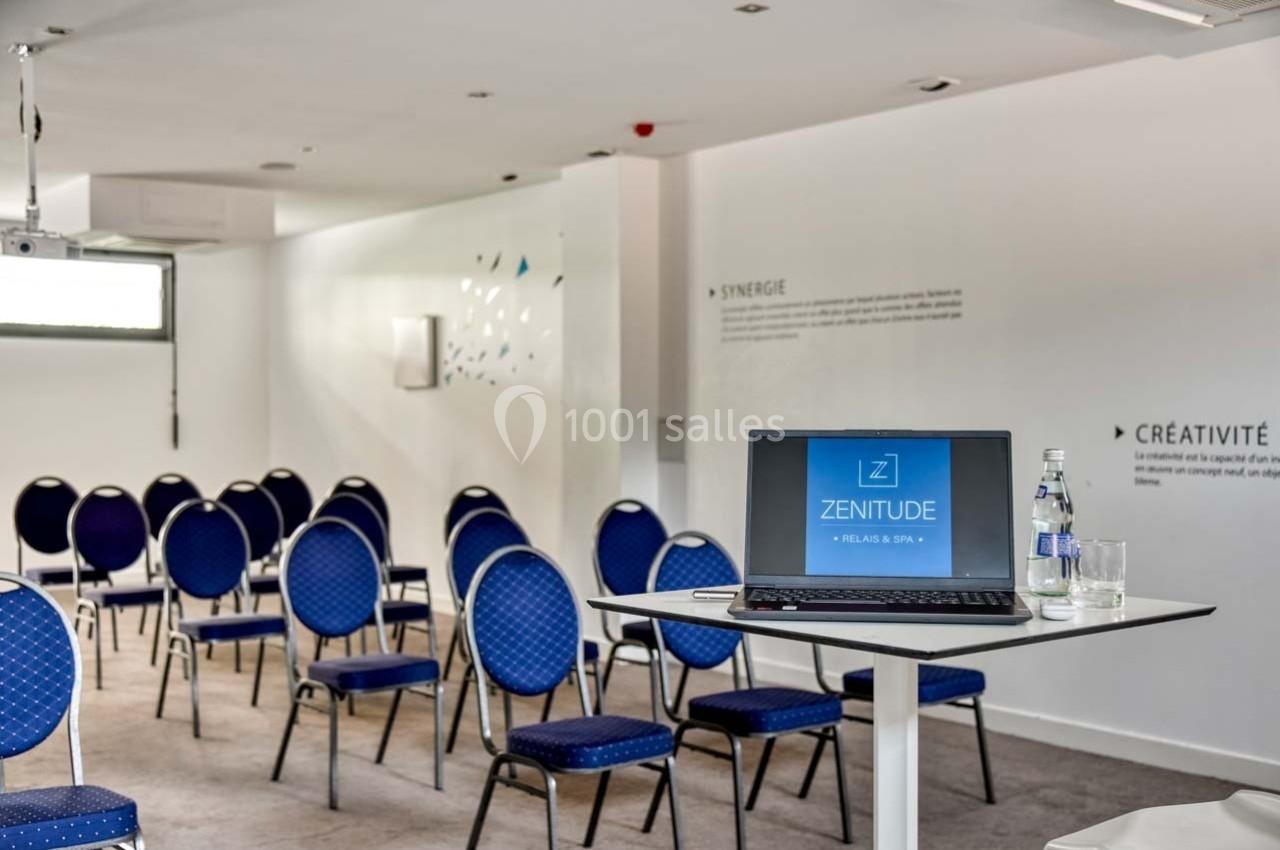 Salle de réunion lumineuse avec chaises bleues, un ordinateur portable sur une table et des inscriptions murales.