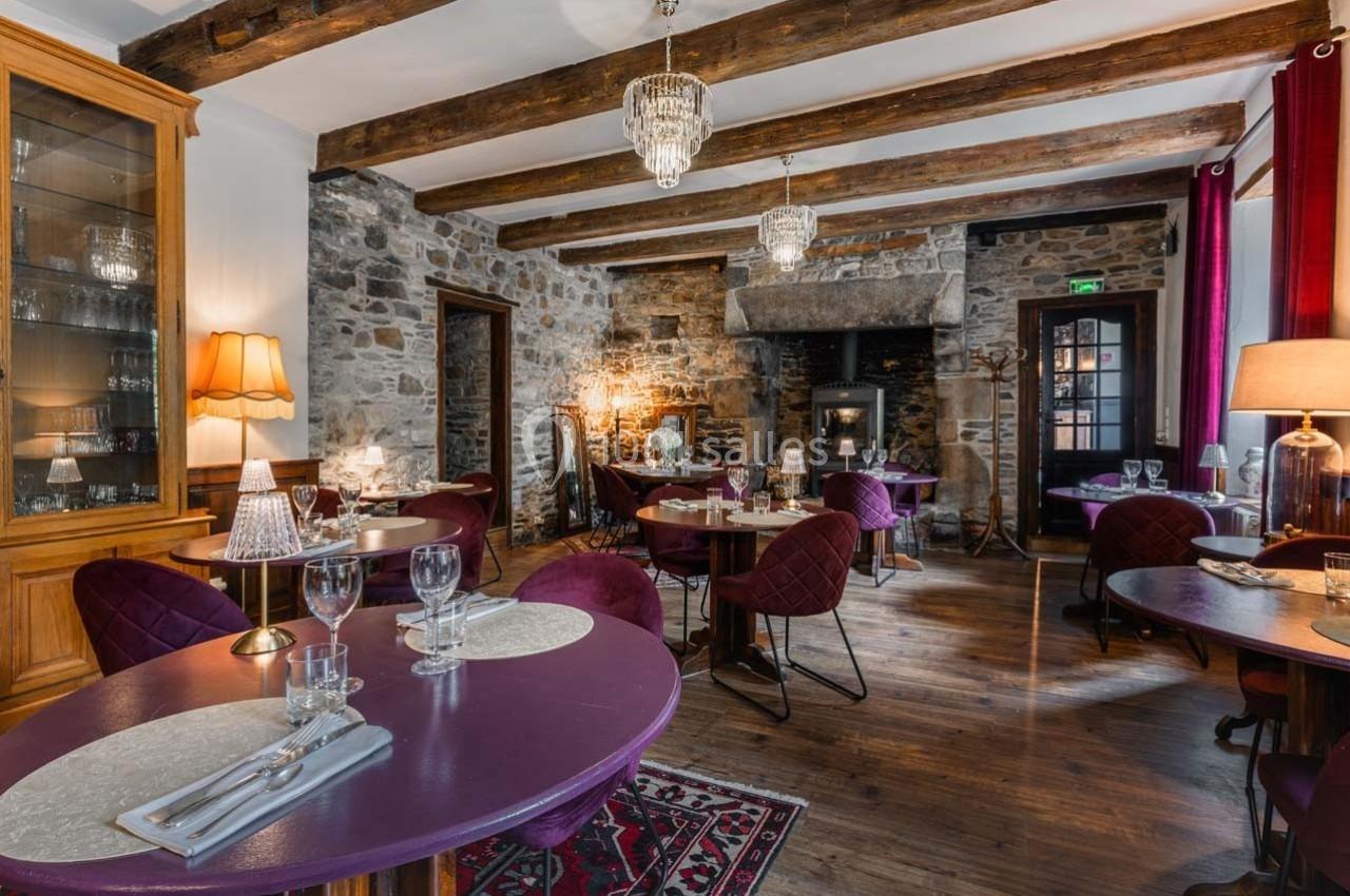 Salle de restaurant chaleureuse avec murs en pierre, poutres apparentes, tables dressées et éclairage tamisé.