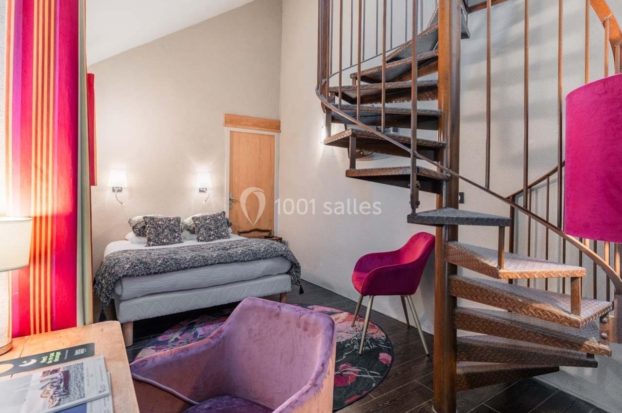 Chambre avec lit double, fauteuils colorés, escalier en colimaçon en bois et décoration chaleureuse.