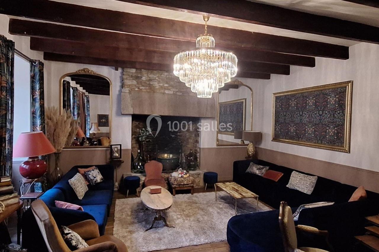 Salon chaleureux avec poutres apparentes, cheminée en pierre, lustre en cristal et mobilier éclectique.