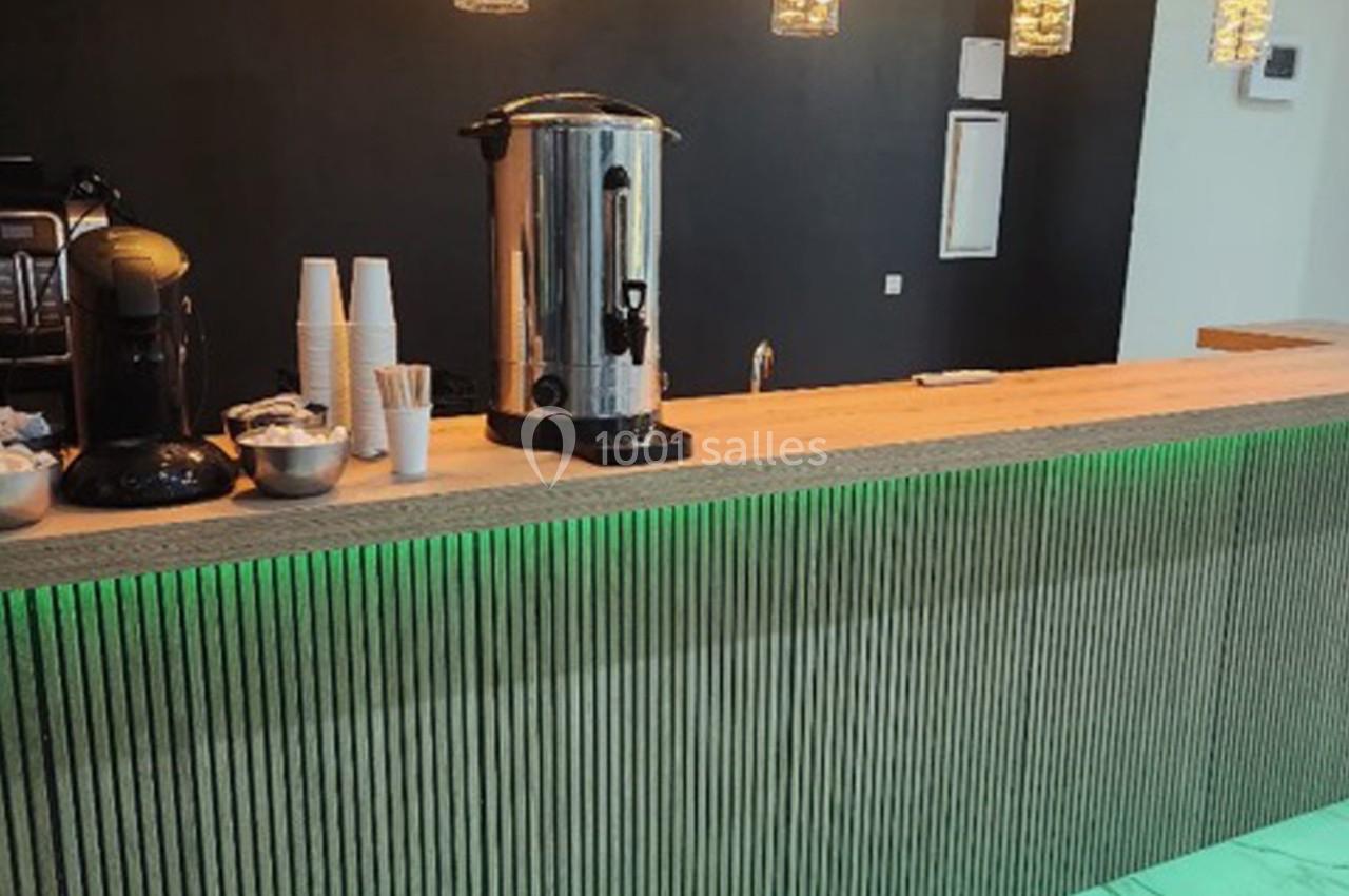 Comptoir en bois avec une machine à café, des gobelets et un éclairage vert en dessous.