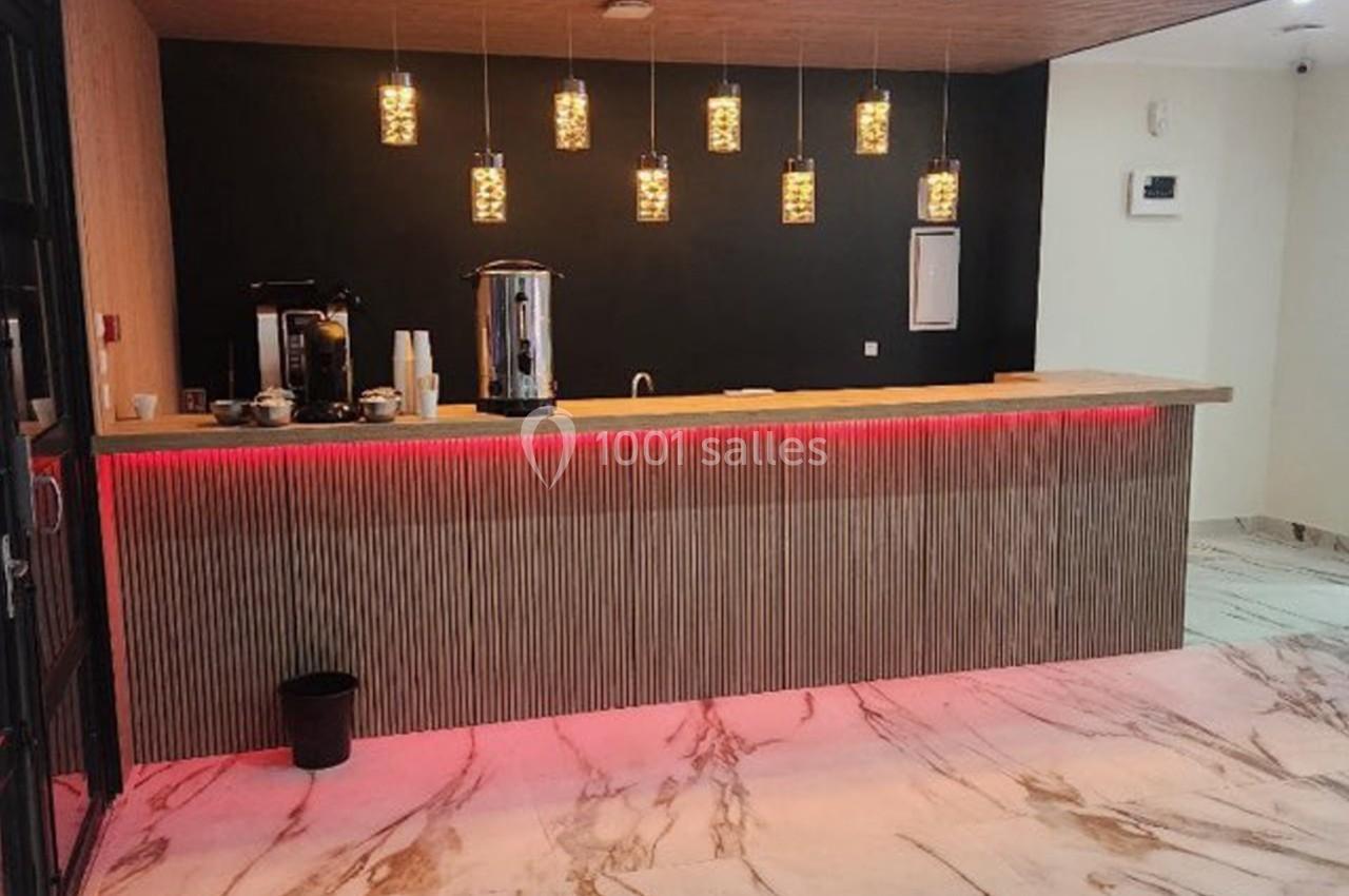 Comptoir en bois avec éclairage rouge, cafetière et distributeur d'eau, dans un espace au sol en marbre.