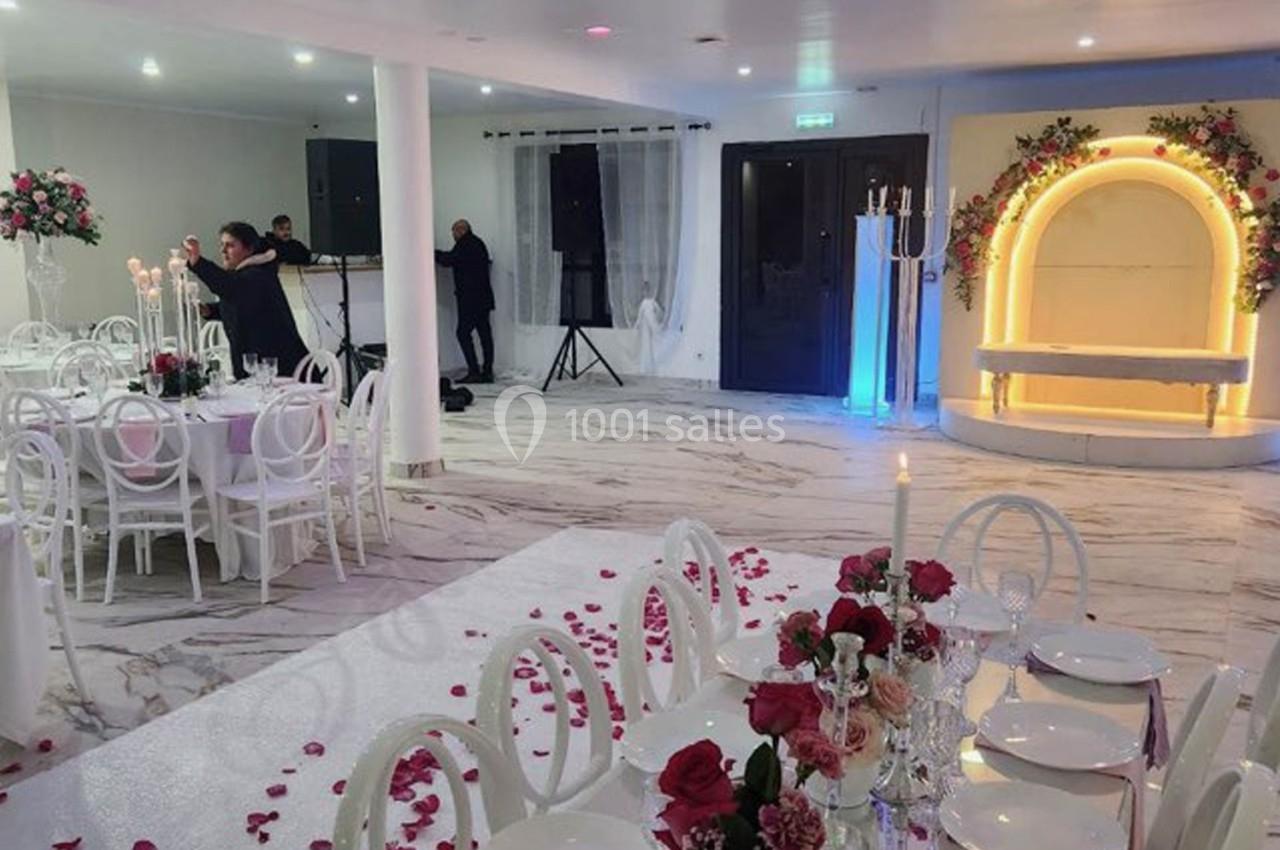 Salle de réception décorée avec des tables élégantes, des chaises blanches, des fleurs et un éclairage chaleureux.