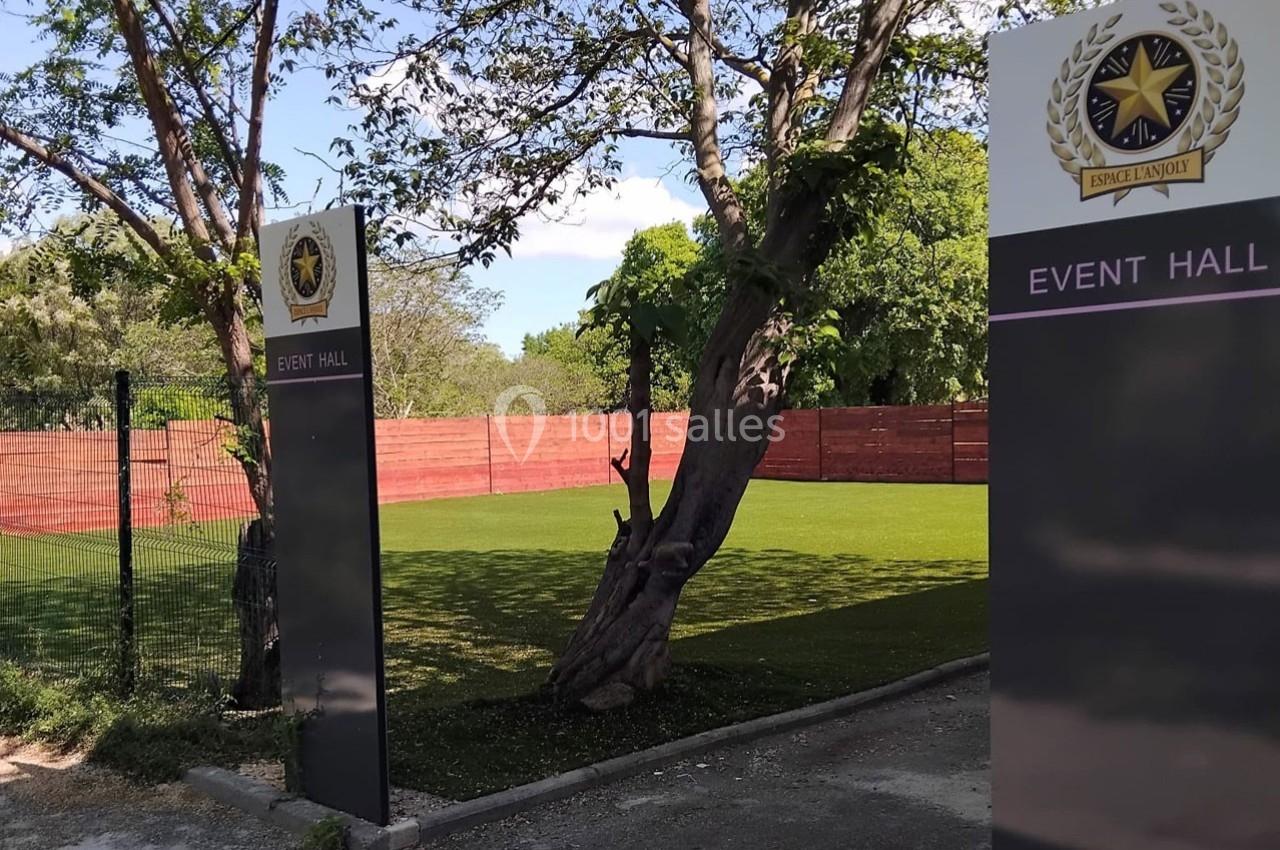 Entrée d'une salle d'événements avec panneaux signalétiques, pelouse et clôture en bois rouge en arrière-plan.