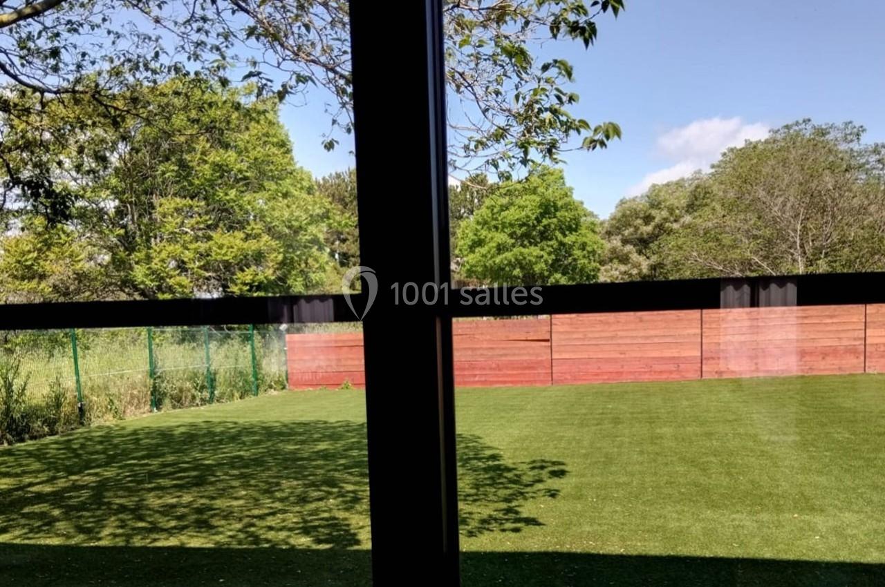 Vue depuis une fenêtre sur un jardin avec pelouse, clôtures en bois et végétation sous un ciel partiellement dégagé.