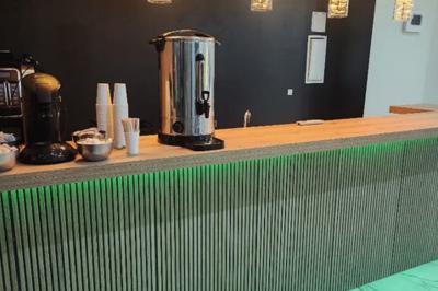 Comptoir en bois éclairé par des suspensions, avec machines à café et sol en marbre dans un espace moderne.