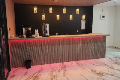 Comptoir en bois éclairé par des suspensions, avec machines à café et sol en marbre dans un espace moderne.