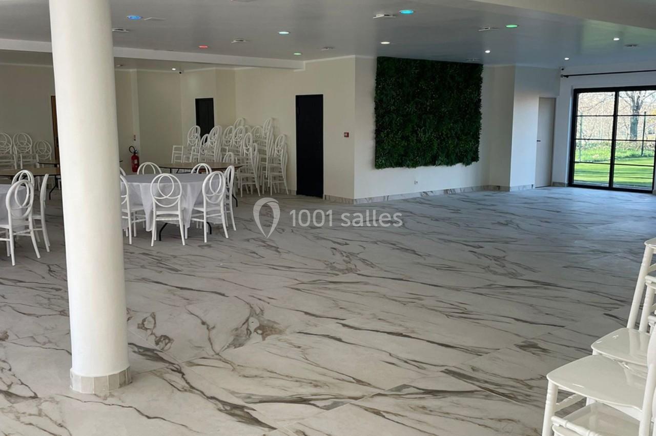 Salle lumineuse avec sol en marbre, chaises blanches empilées, mur végétal et grandes baies vitrées donnant sur l'extérieur.