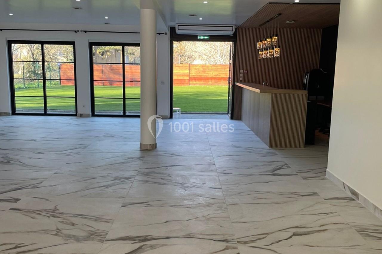 Salle lumineuse avec sol en marbre, comptoir en bois, grandes baies vitrées donnant sur un espace extérieur verdoyant.