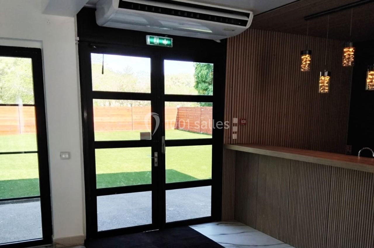 Porte vitrée donnant sur un espace extérieur avec pelouse, située dans une pièce lumineuse au sol en marbre.