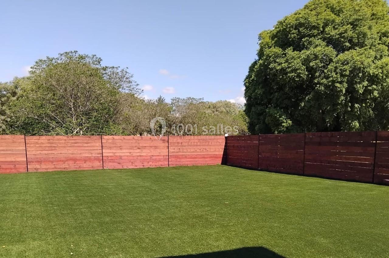 Pelouse verte bien entretenue entourée de clôtures en bois rouge et d'arbres sous un ciel dégagé.