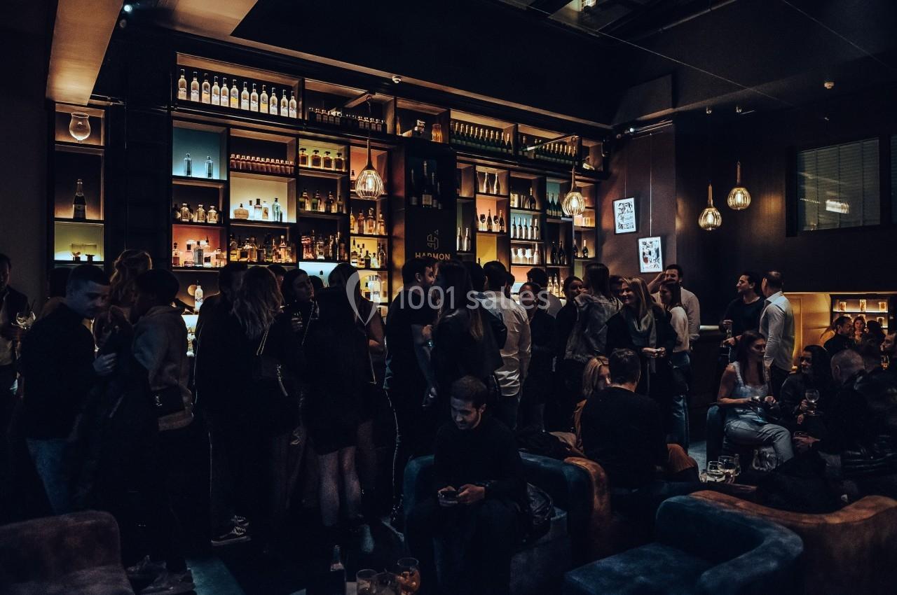 Groupe de personnes rassemblées dans un bar à l'ambiance tamisée, avec des étagères remplies de bouteilles en arrière-plan.
