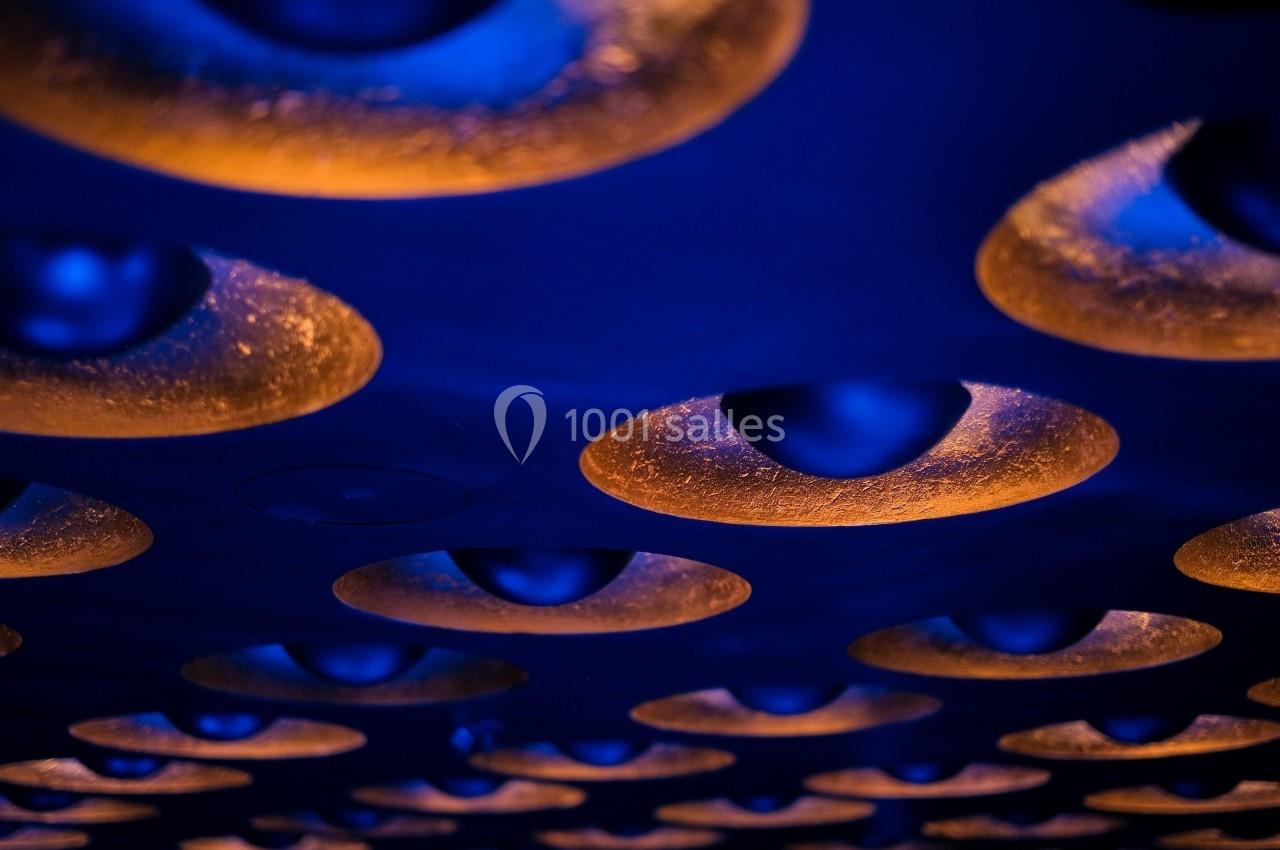 Plafond avec des luminaires circulaires émettant une lumière orange, contrastant avec un éclairage bleu.