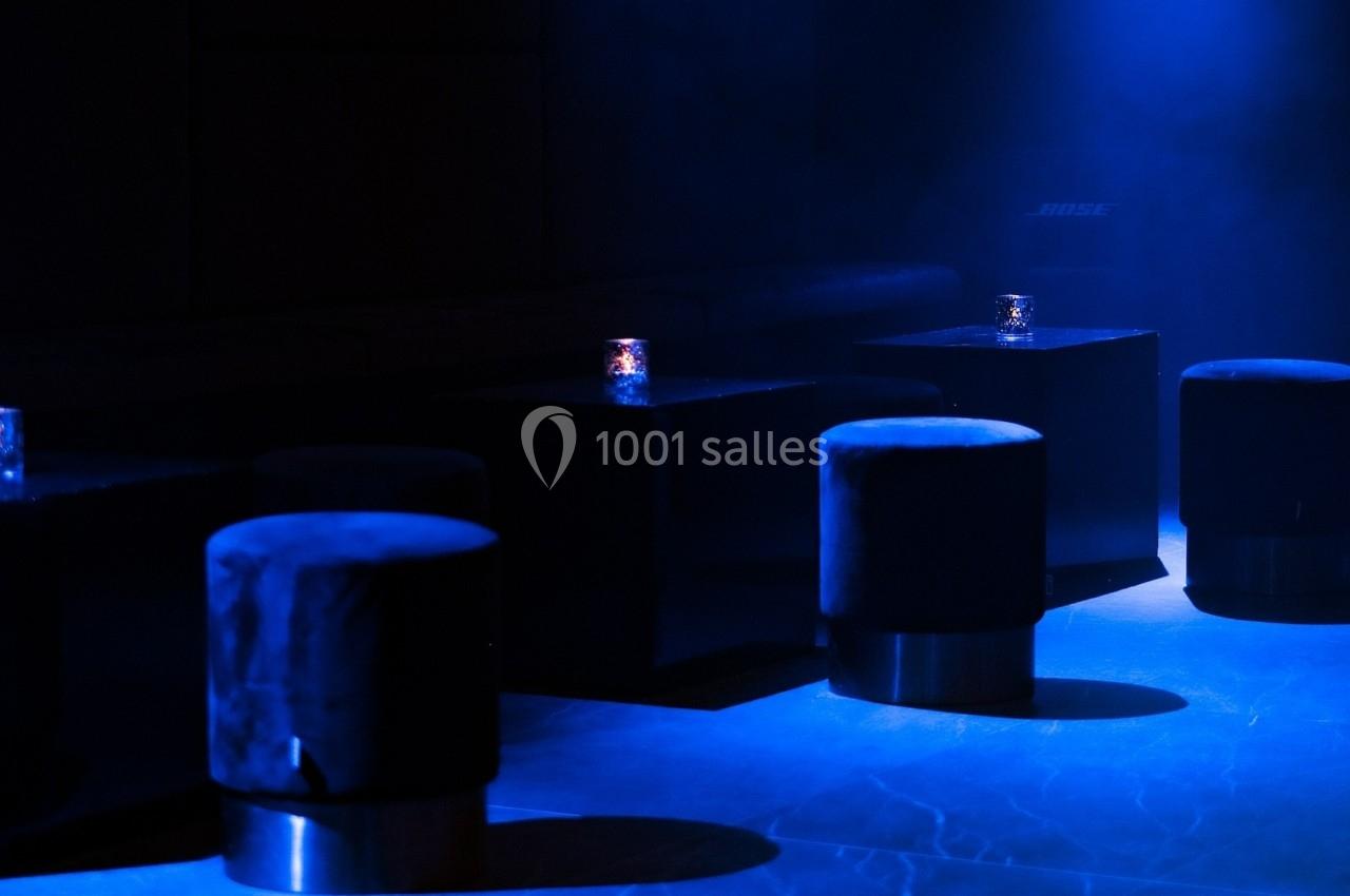 Tabourets noirs et tables basses éclairés par une lumière bleue tamisée dans un espace sombre.