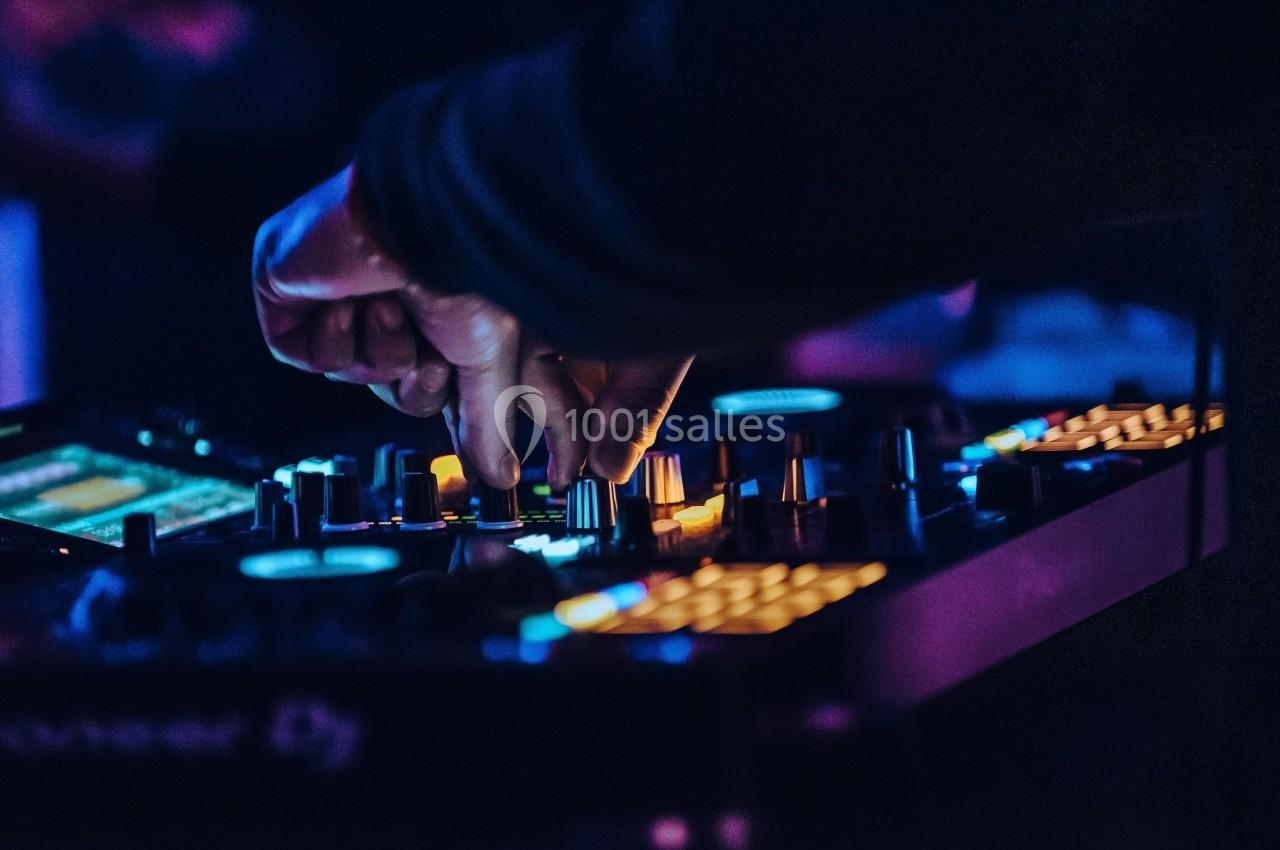 Main ajustant des commandes sur une table de mixage éclairée dans une ambiance lumineuse tamisée.