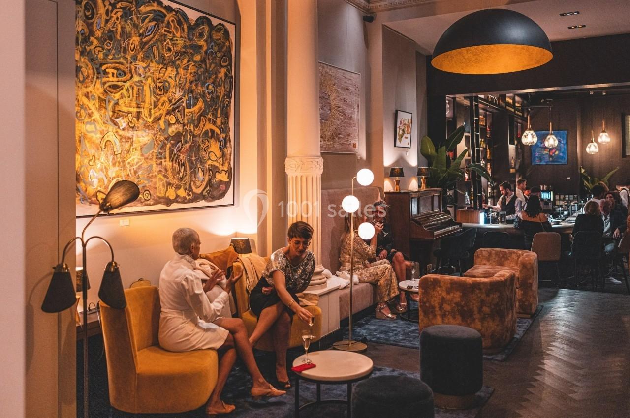 Salon chaleureux avec canapés, œuvres d'art au mur, éclairage tamisé et personnes discutant autour de tables.