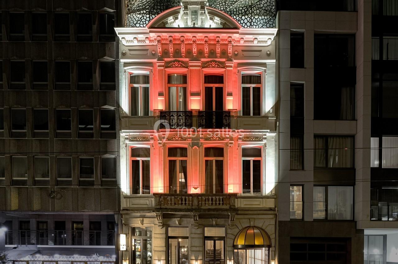 Façade d'un bâtiment ancien éclairé en rouge et blanc, entouré d'immeubles modernes, de nuit.