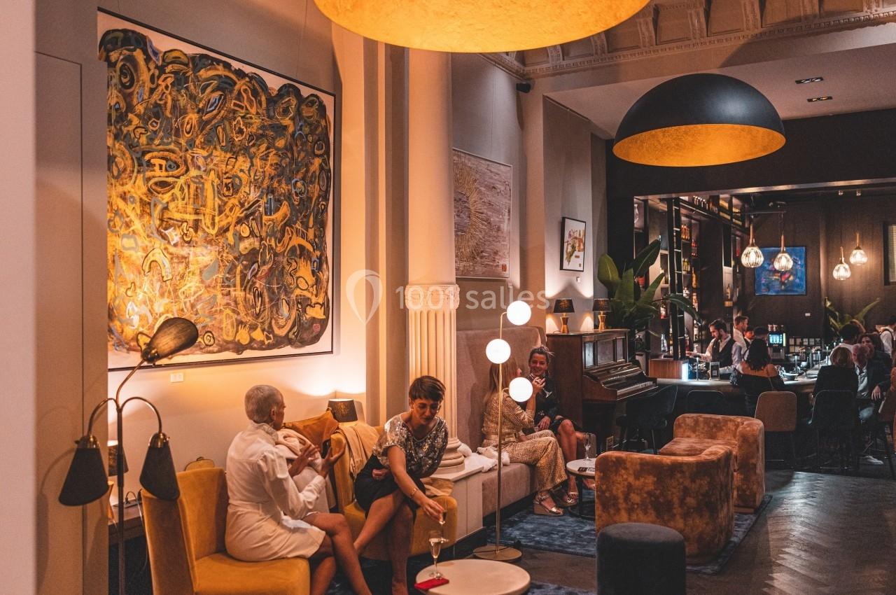 Personnes discutant dans un salon chaleureux avec des œuvres d'art au mur, éclairé par des lampes suspendues.