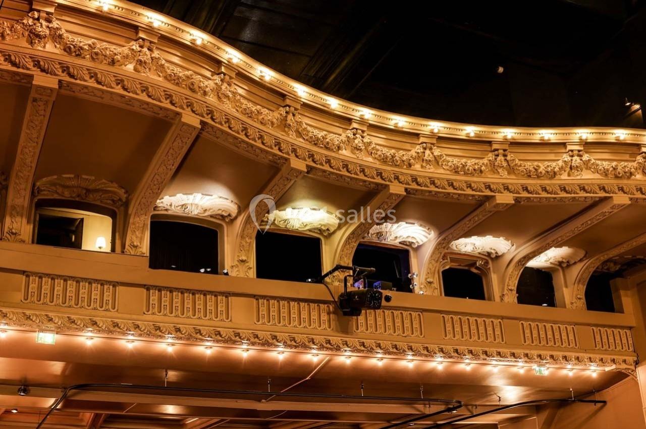 Balcon d'un théâtre avec des ornements détaillés, éclairé par des lumières chaudes dans une ambiance nocturne.