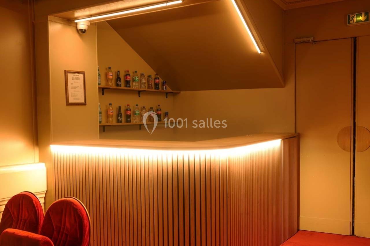 Comptoir de bar en bois éclairé, avec étagères contenant des bouteilles, dans un intérieur au ton chaleureux.