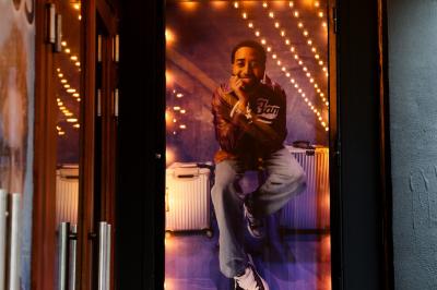 Salle avec moquette rouge, table en bois clair, chaises rouges et miroir éclairé par des ampoules.
