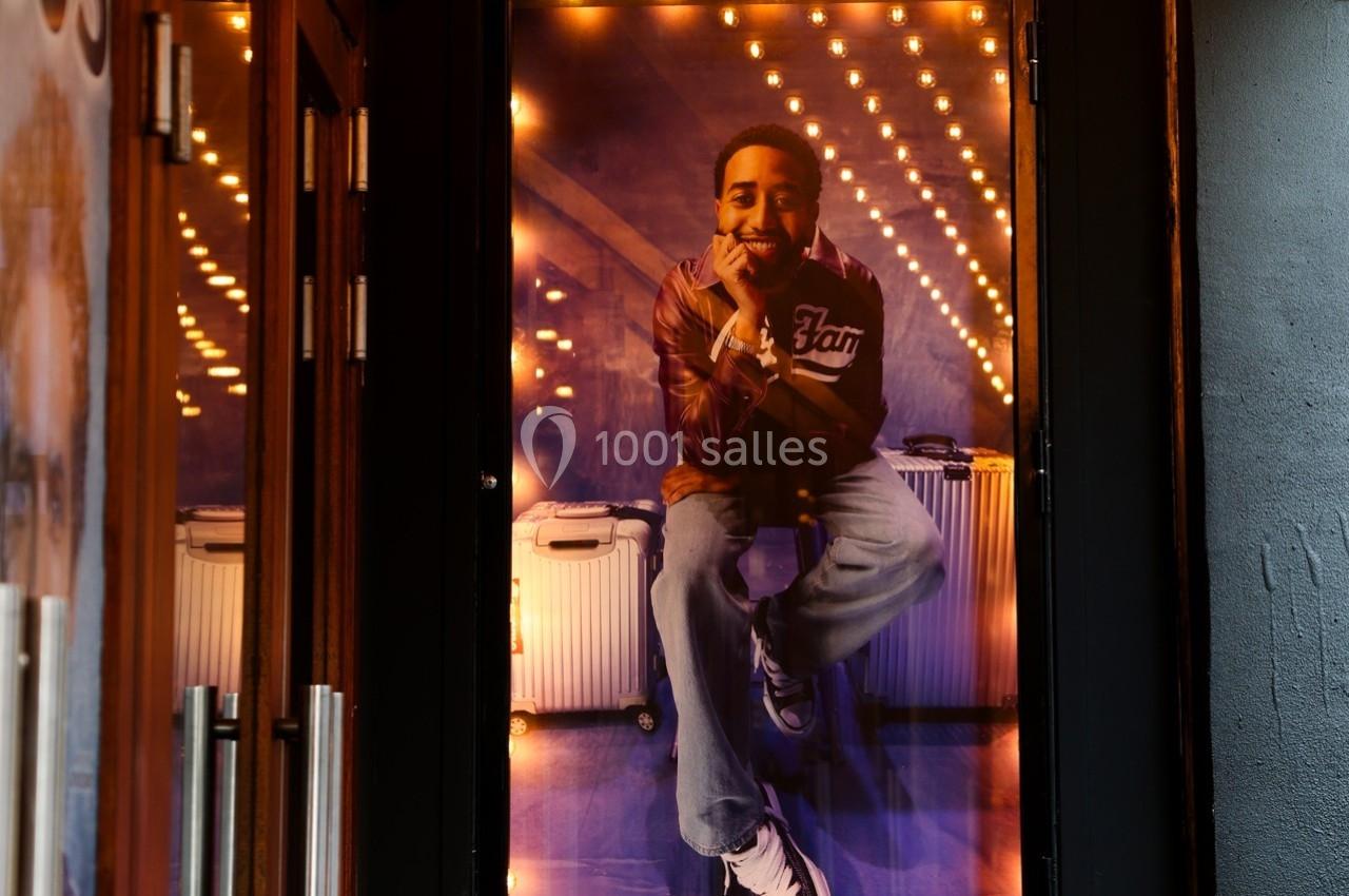 Portrait d'un homme souriant, assis devant des valises, éclairé par des guirlandes lumineuses en arrière-plan.