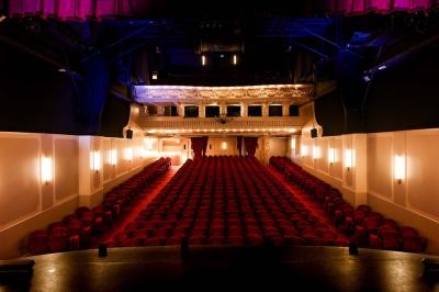 Salle avec moquette rouge, table en bois clair, chaises rouges et miroir éclairé par des ampoules.