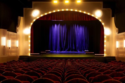Salle avec moquette rouge, table en bois clair, chaises rouges et miroir éclairé par des ampoules.