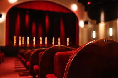Salle avec moquette rouge, table en bois clair, chaises rouges et miroir éclairé par des ampoules.
