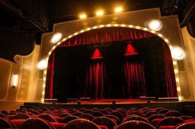 Salle avec moquette rouge, table en bois clair, chaises rouges et miroir éclairé par des ampoules.