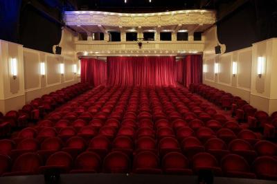Salle avec moquette rouge, table en bois clair, chaises rouges et miroir éclairé par des ampoules.