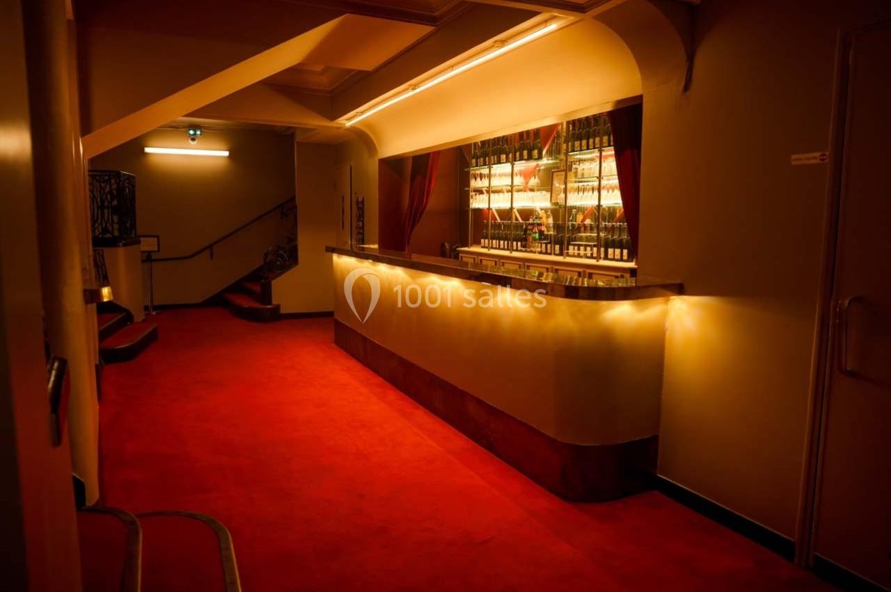 Un hall avec tapis rouge, comptoir éclairé et escalier en arrière-plan dans une ambiance tamisée.