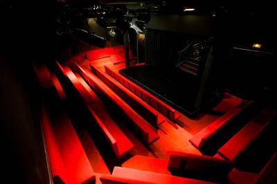 Salle avec moquette rouge, table en bois clair, chaises rouges et miroir éclairé par des ampoules.