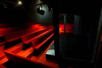 Salle avec moquette rouge, table en bois clair, chaises rouges et miroir éclairé par des ampoules.