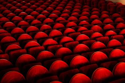 Salle avec moquette rouge, table en bois clair, chaises rouges et miroir éclairé par des ampoules.