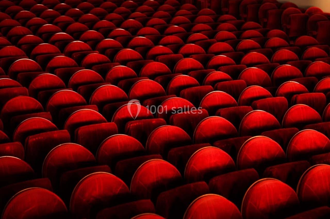 Rangées de sièges en velours rouge alignées dans une salle de spectacle vide.