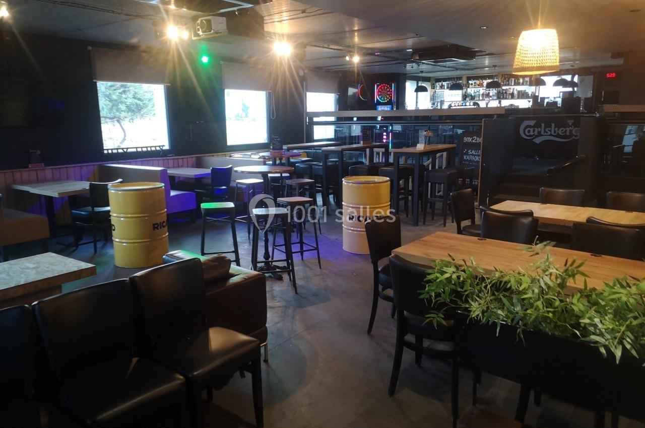 Salle de bar avec tables, chaises, tonneaux décoratifs et éclairage tamisé.