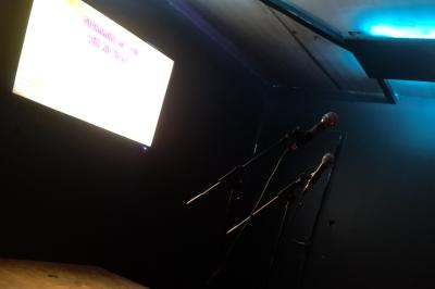 Deux micros sur scène dans une salle sombre, avec un écran lumineux affichant du texte en arrière-plan.